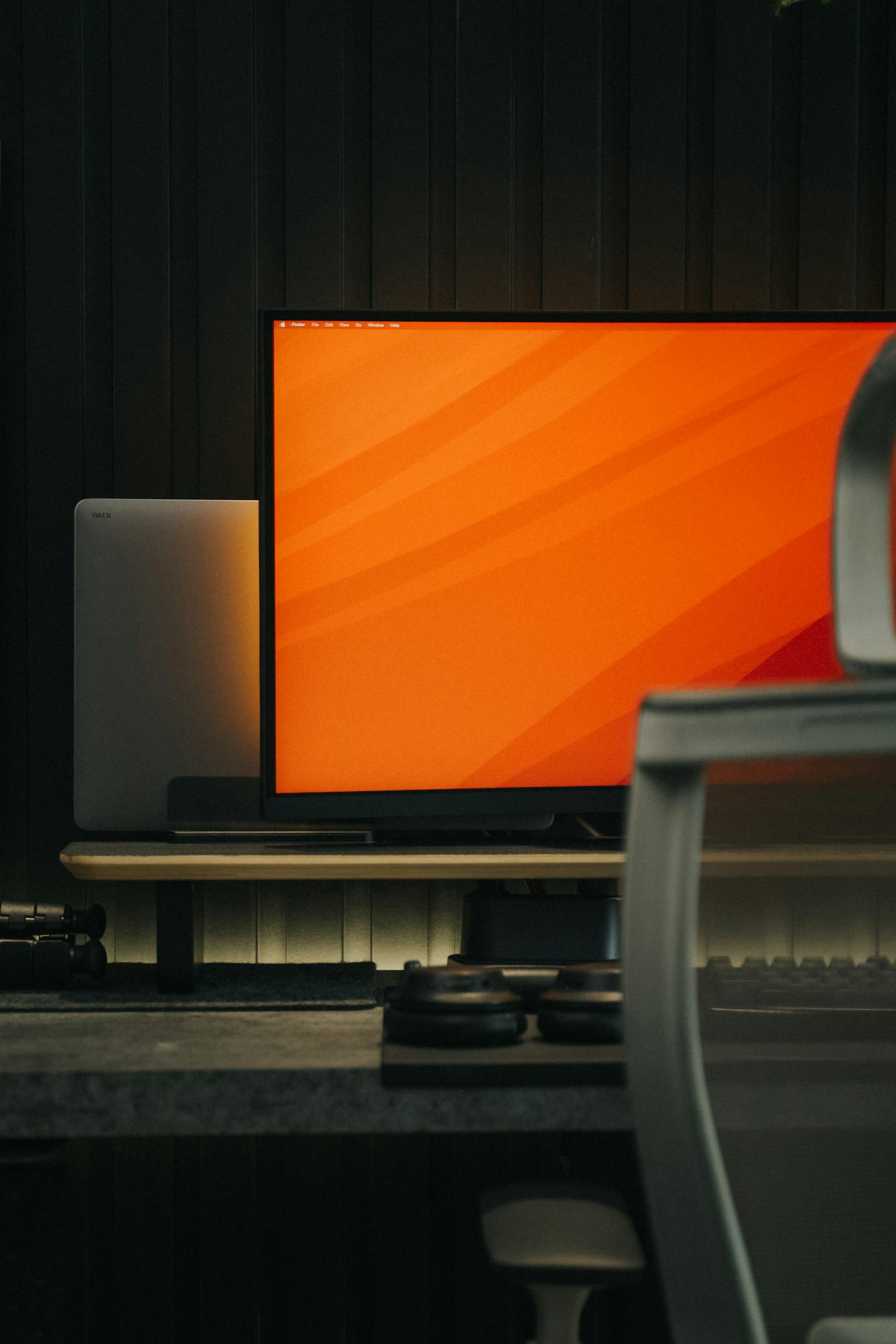 A stylish indoor workspace featuring a monitor with an orange screen, ideal for tech setups.