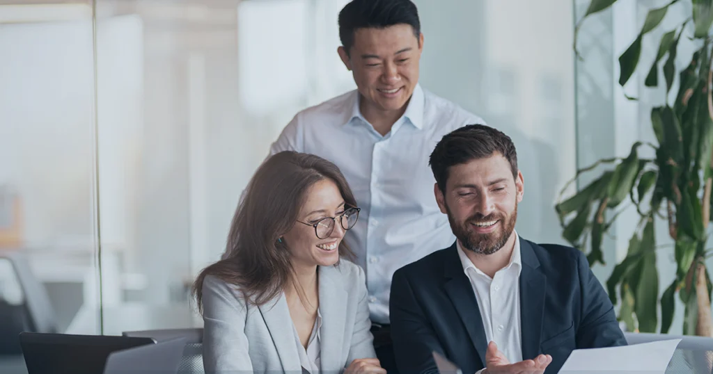 Three people looking at computer in office setting.