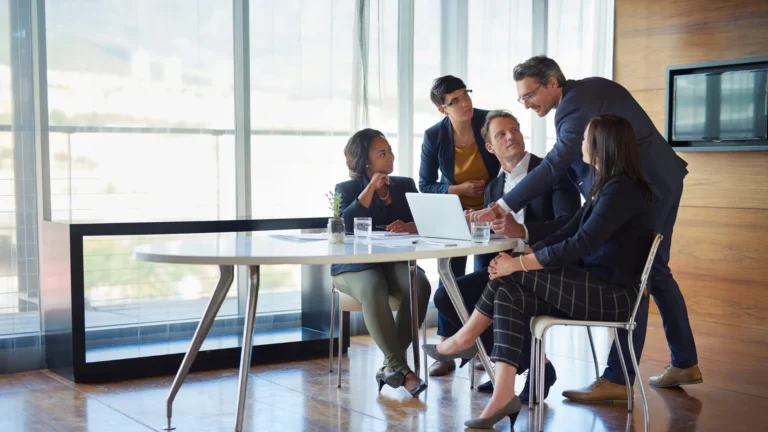 Business team gathered around a laptop in a glass-walled meeting room