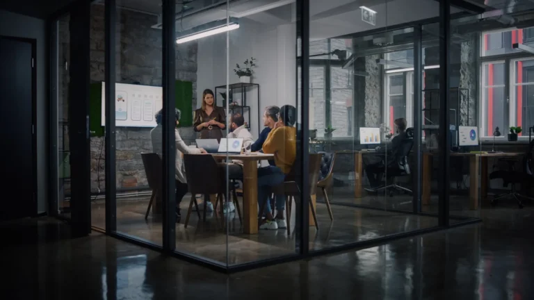 Team meeting in a glass-walled office with charts on the wall screen