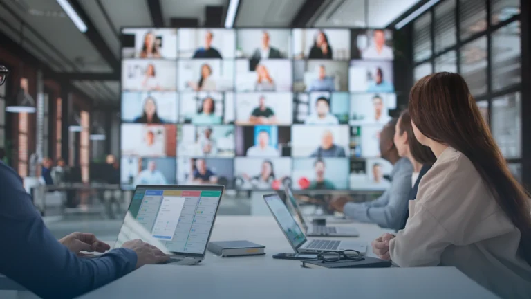 Team in a conference room facing a wall of video call participants