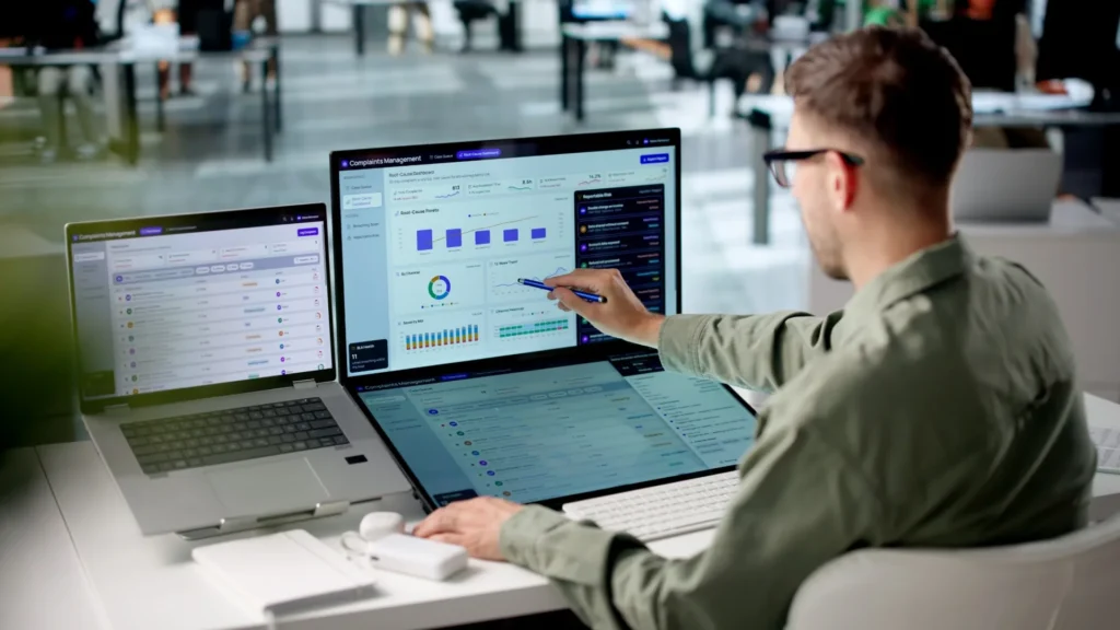 Analyst pointing at a compliance dashboard across two laptop screens