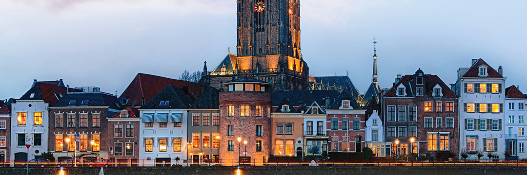 Dutch riverside houses and a church tower lit at dusk