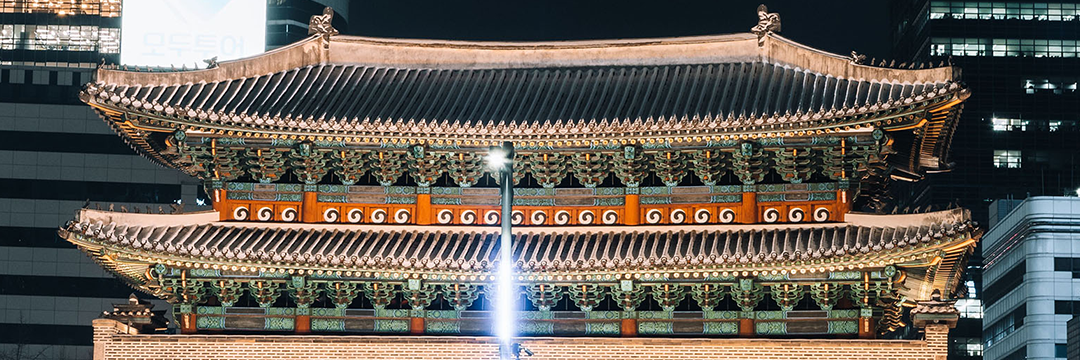 Traditional Korean palace gate lit at night among office towers